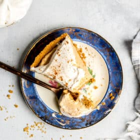 Slice of pumpkin mousse pie on a blue bordered plate with a white center with a copper fork with a spoonful of pie on the fork.