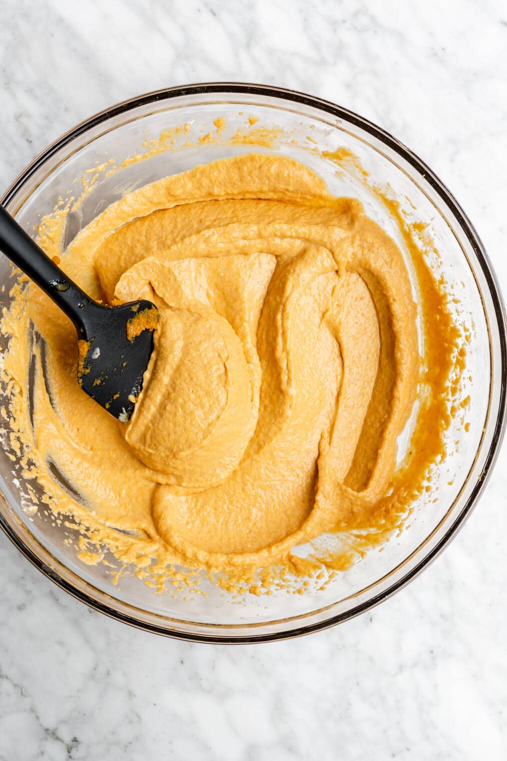 Pumpkin mousse ingredients smoothed in a glass mixing bowl with a black spatula.