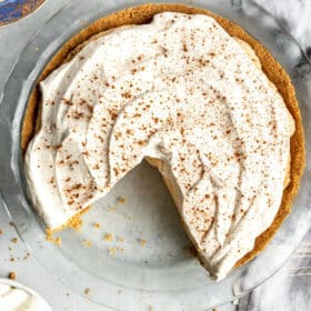 Pumpkin mousse pie with slice removed on a grey and white marble surface with linen draped around the pie dish.