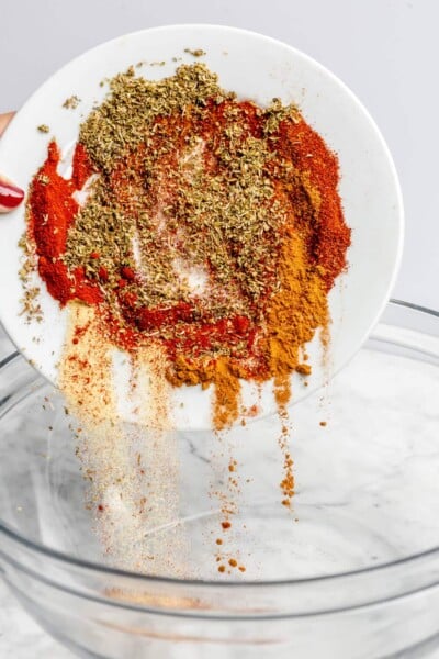 Hand pouring plate of spices into a glass bowl.