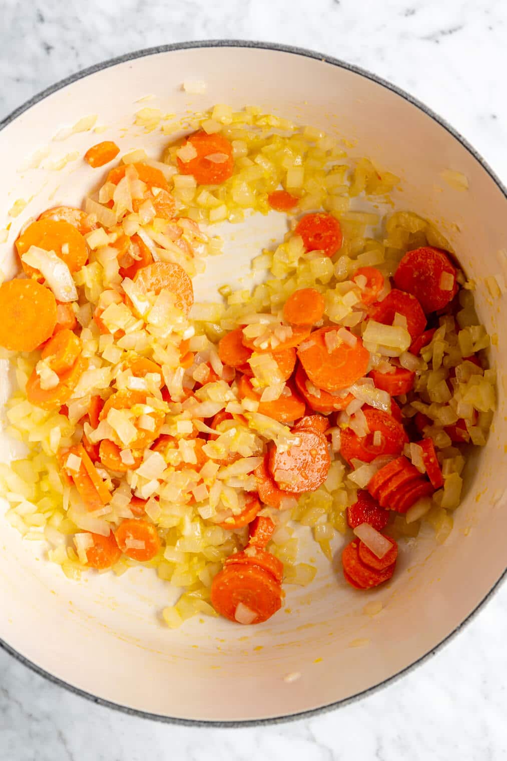 Top down view of carrots and onions mixed with spices in a white pot.