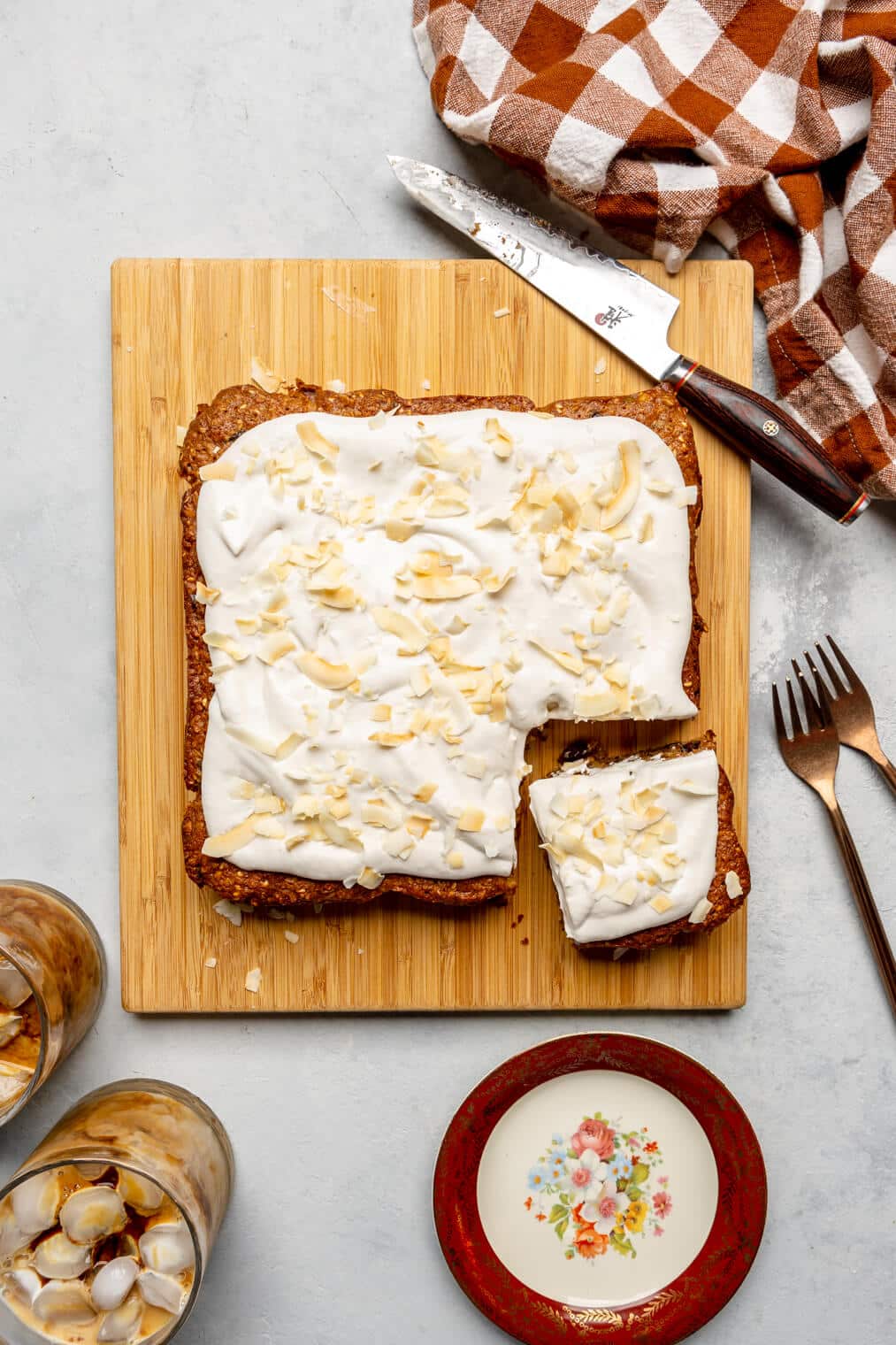 Oatmeal breakfast cake with a corner cut out, topped with coconut whipped cream and coconut flakes on a wooden cutting board.