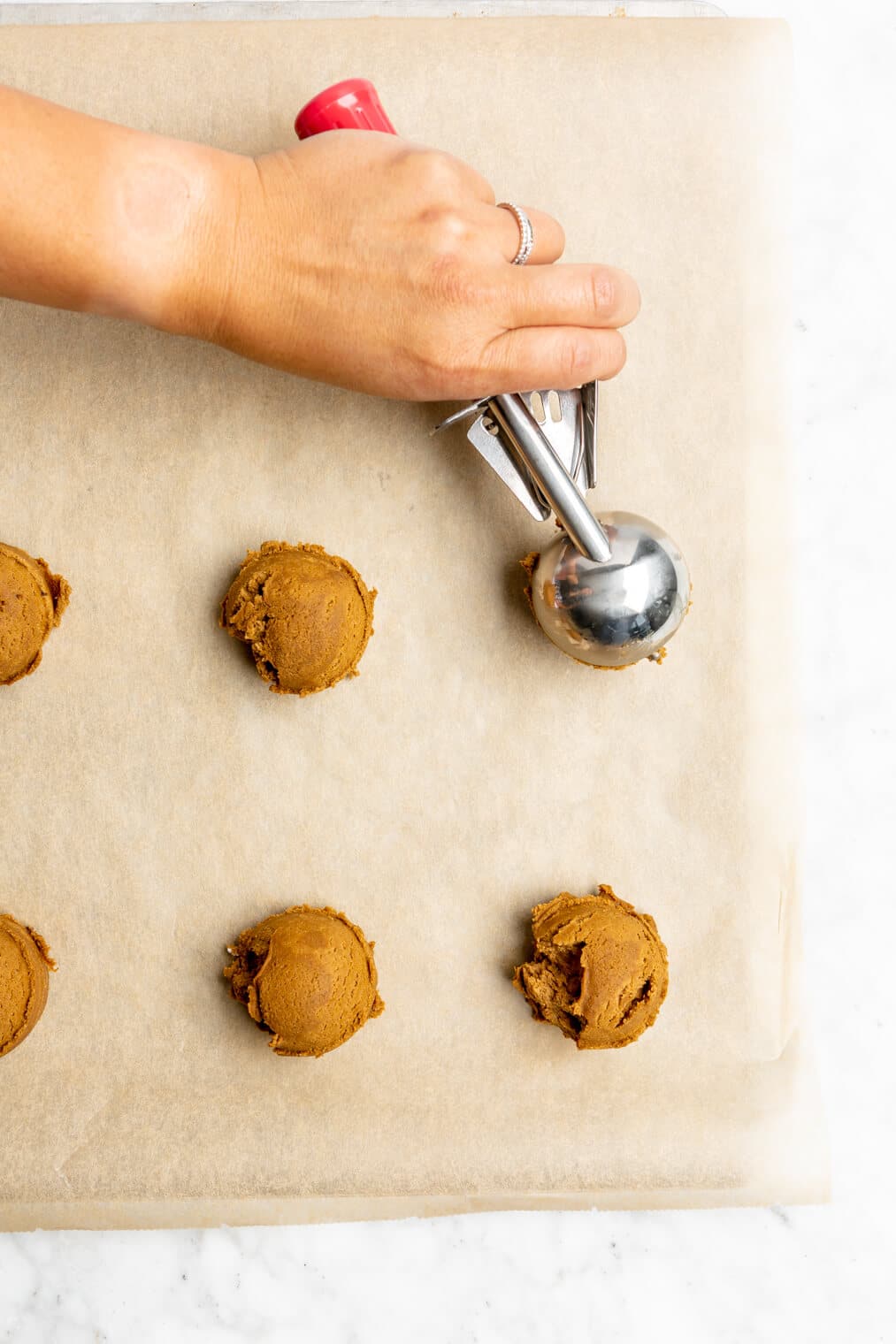 Top down view of cookies being scooped onto a parchment lined baking sheet.