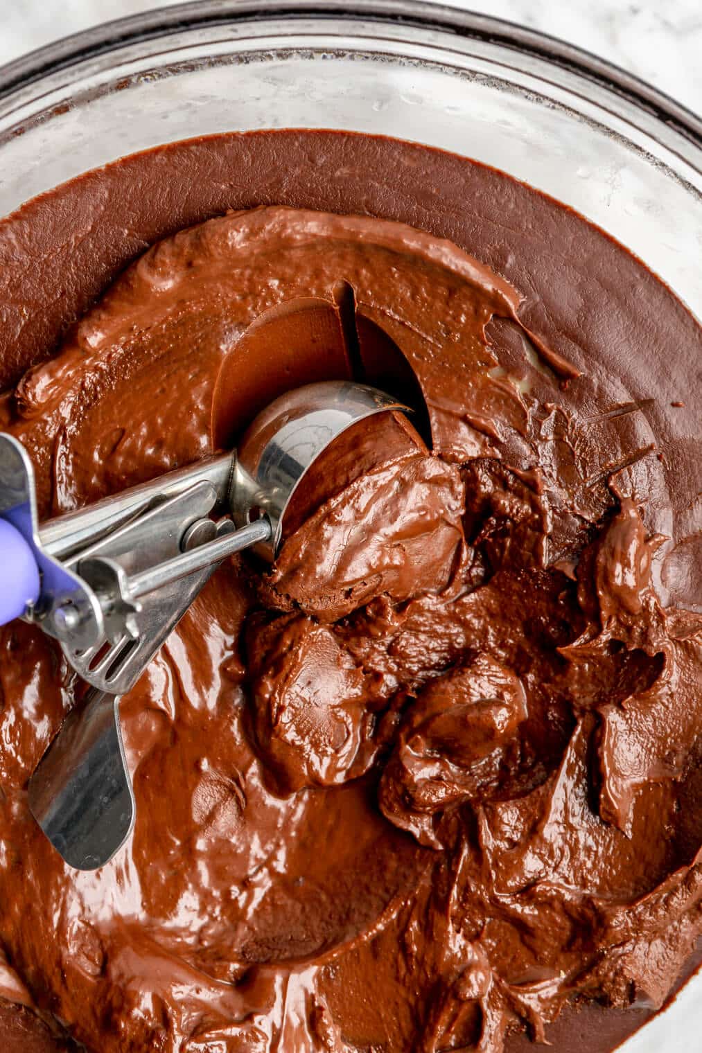 Cookie scoop scooping chocolate ganache out of a bowl.