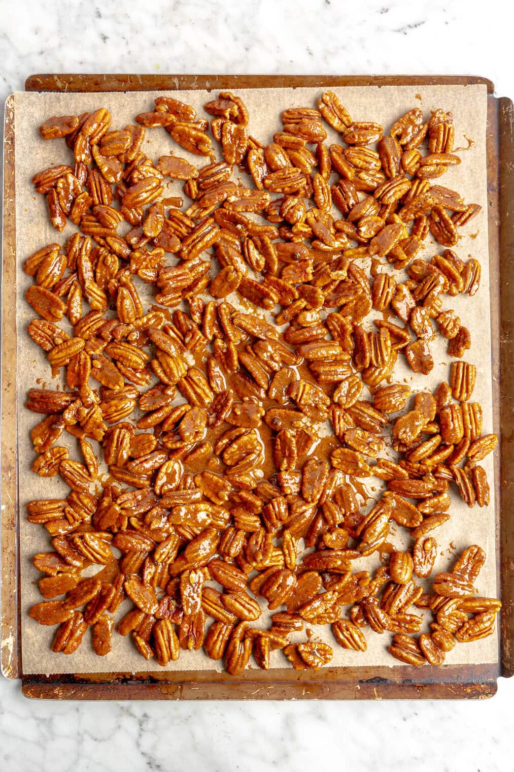 Candied pecan mixture spread out on a parchment lined baking sheet.