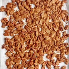 Top down photo of candied pecans on a baking sheet lined with white parchment paper.