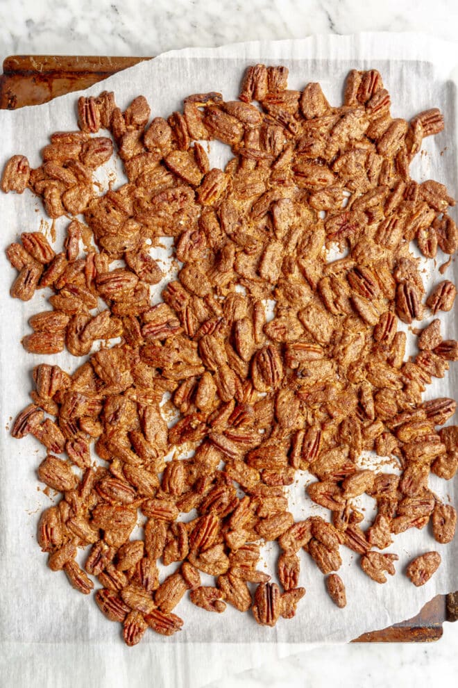 Top down photo of candied pecans on a baking sheet lined with white parchment paper.