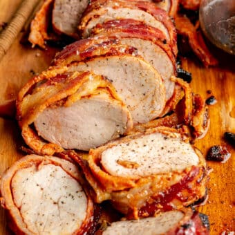 Close up of sliced bacon wrapped pork tenderloin on a cutting board.