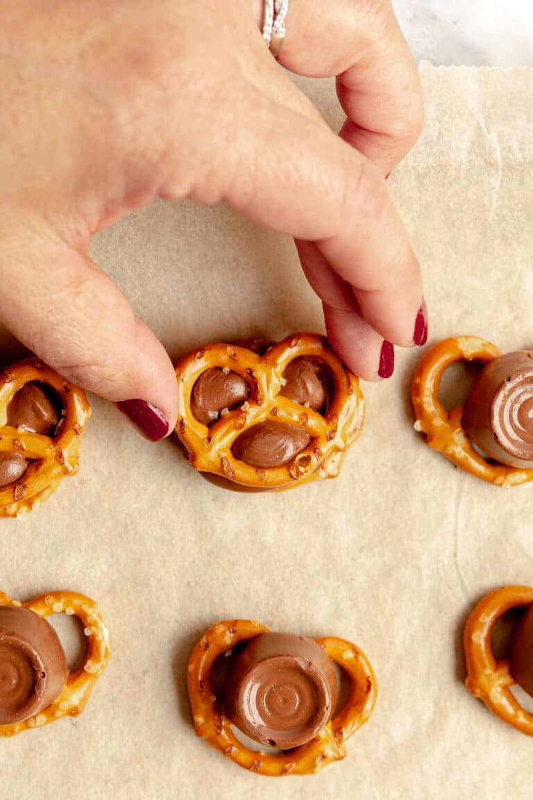 Hand pressing a pretzel onto the top of softened rolo candy.