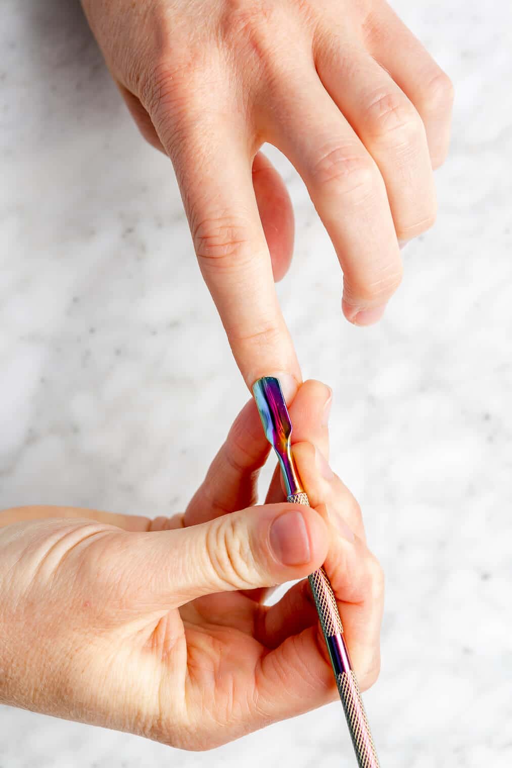Hand holding cuticle tool pushing back cuticles on other hand.