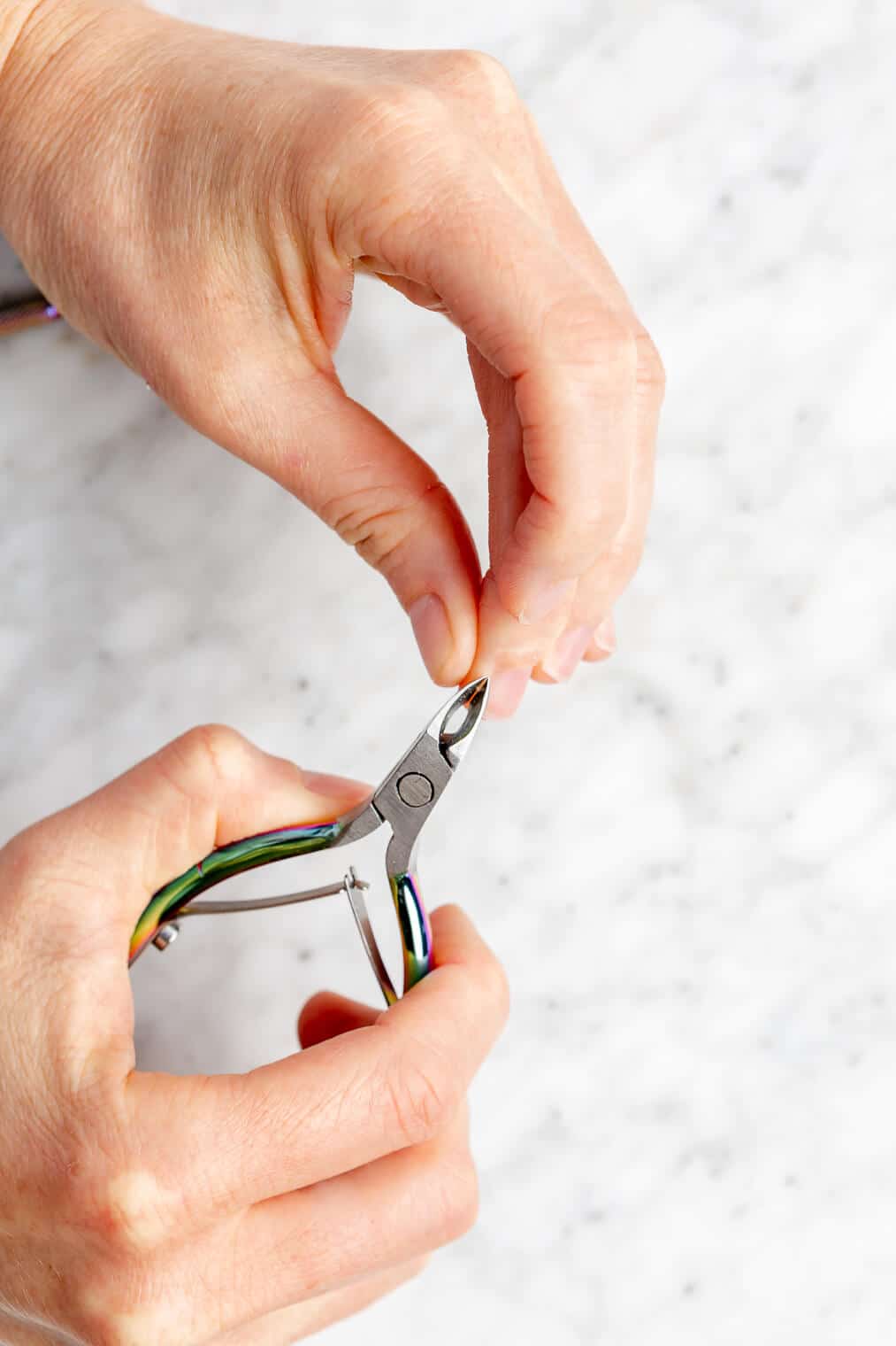 Hands trimming cuticles with cuticle trimmer.
