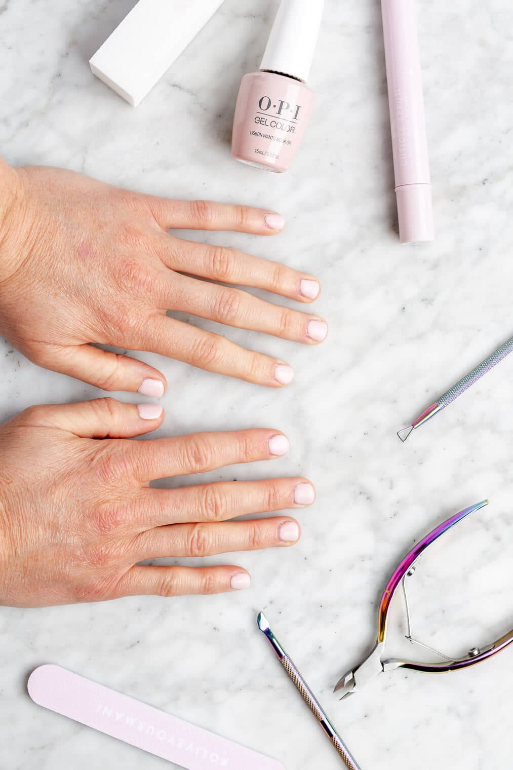 Hands with light pink painted nails on a grey and white marble surface surrounded by nail tools.