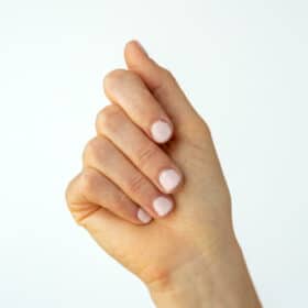 Hand with painted, light pink nails held up against a white backdrop.