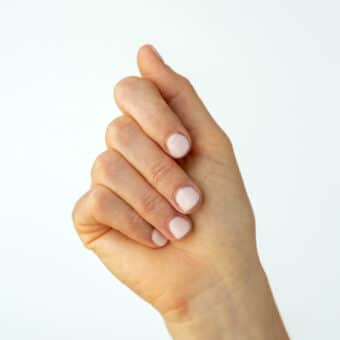 Hand with painted, light pink nails held up against a white backdrop.