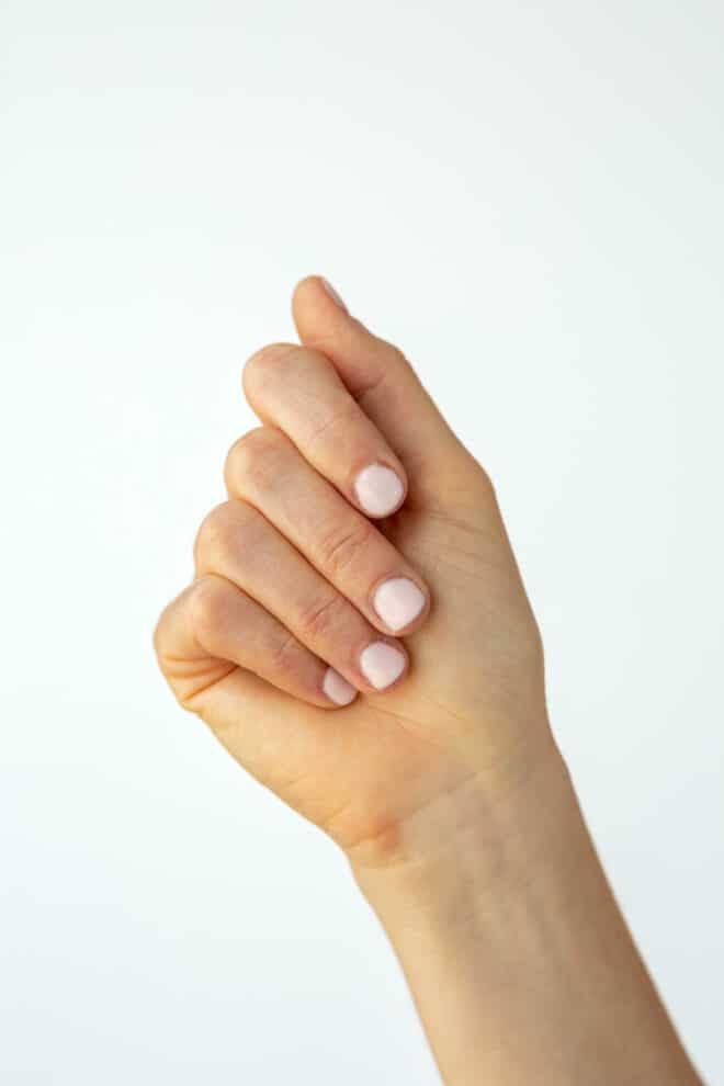 Hand with painted, light pink nails held up against a white backdrop.