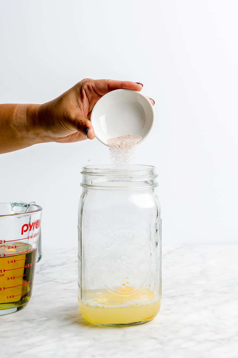 Hand pouring salt into large mason jar over a cracked egg and lemon juice in a large mason jar.