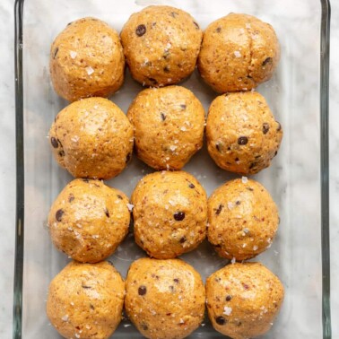 Top down view of 12 protein balls in a glass container on a grey and white marble surface.