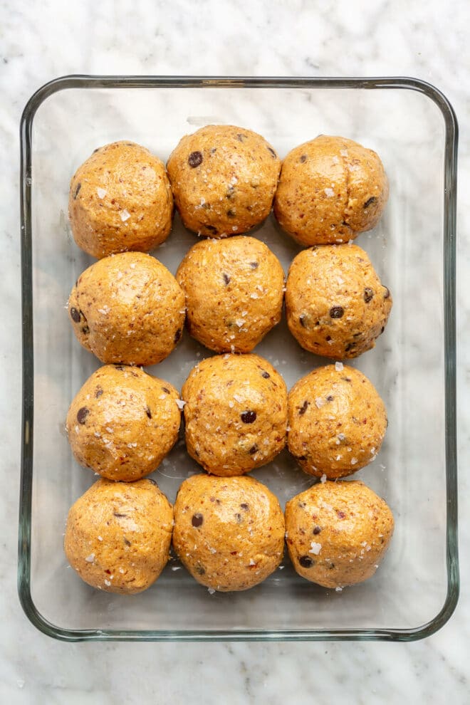 Top down view of 12 protein balls in a glass container on a grey and white marble surface.