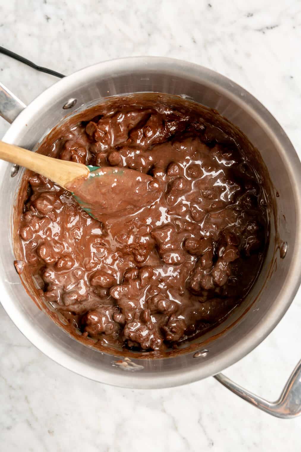 Spoon stirring together melting chocolate chips and sweetened condensed milk in a saucepan.