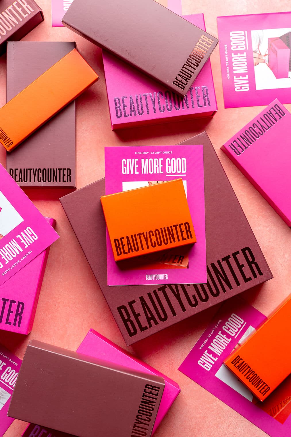 Top down view of Beautycounter limited edition sets in boxes on a pink blush surface. The boxes are of varying sizes and are maroon, red, and bright fuchsia in color.
