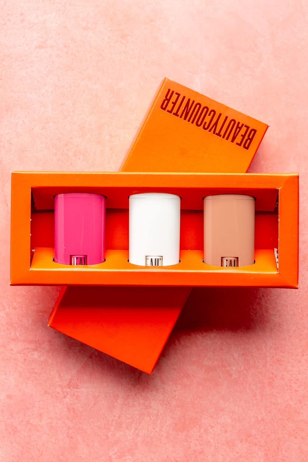 Three rectangle shaped lip balms in a bright red box sitting on a pink blush surface.