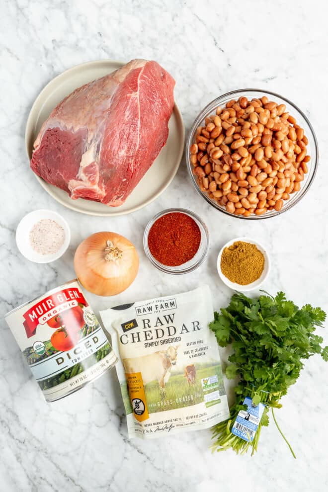 Beef and bean chili ingredients on a grey and white marble surface. 