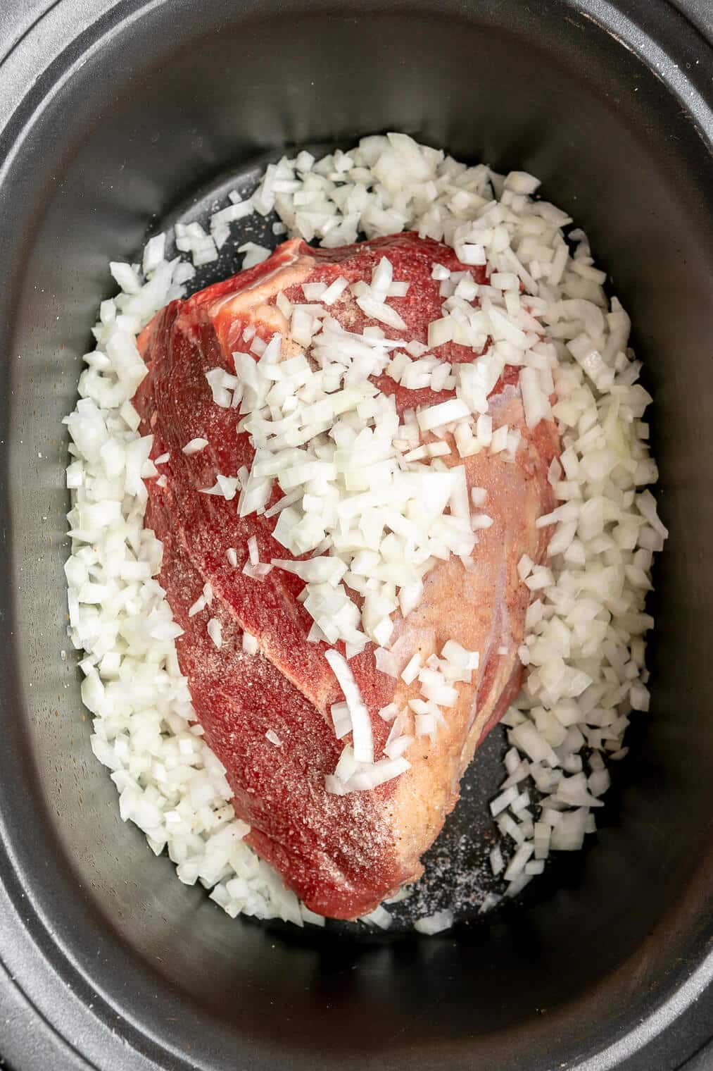 Beef roast topped with diced onion in a crockpot.