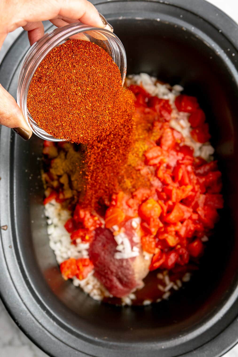 Beef and bean chili seasoning being poured into the crockpot.