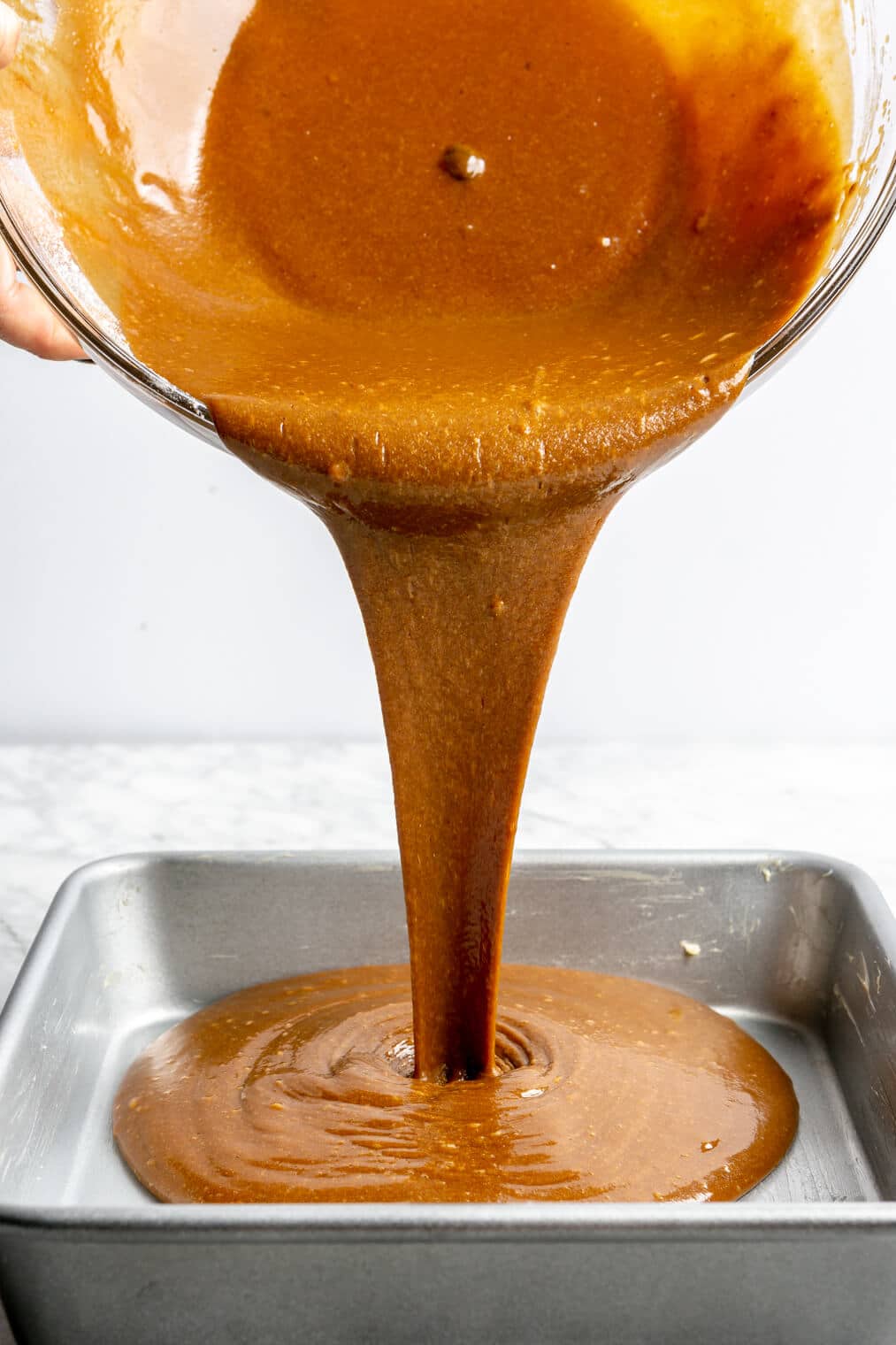 Classic gingerbread batter being poured into an 8x8 metal pan.