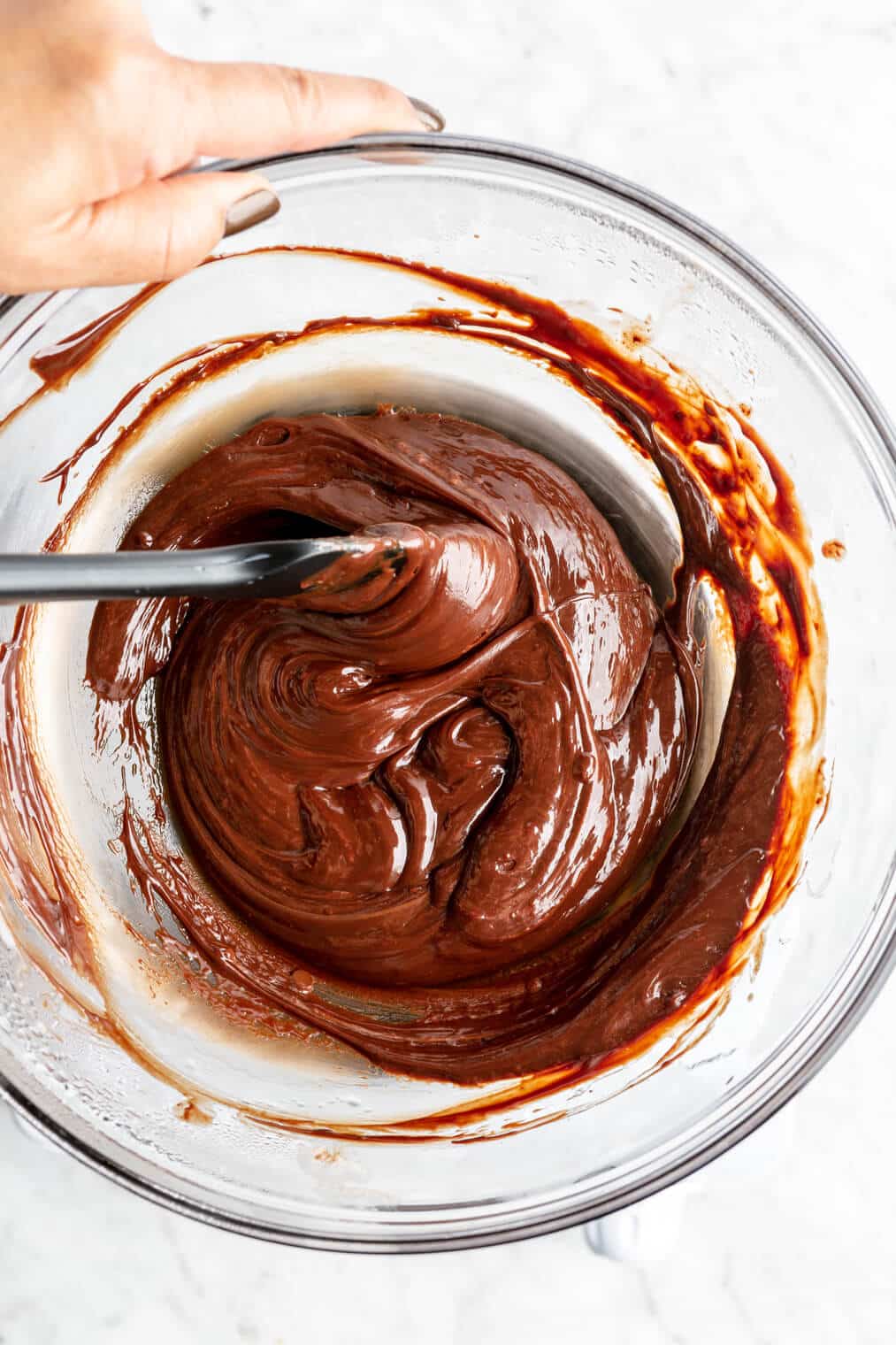 Chocolate melted in a large glass bowl bring stirred with a spatula.
