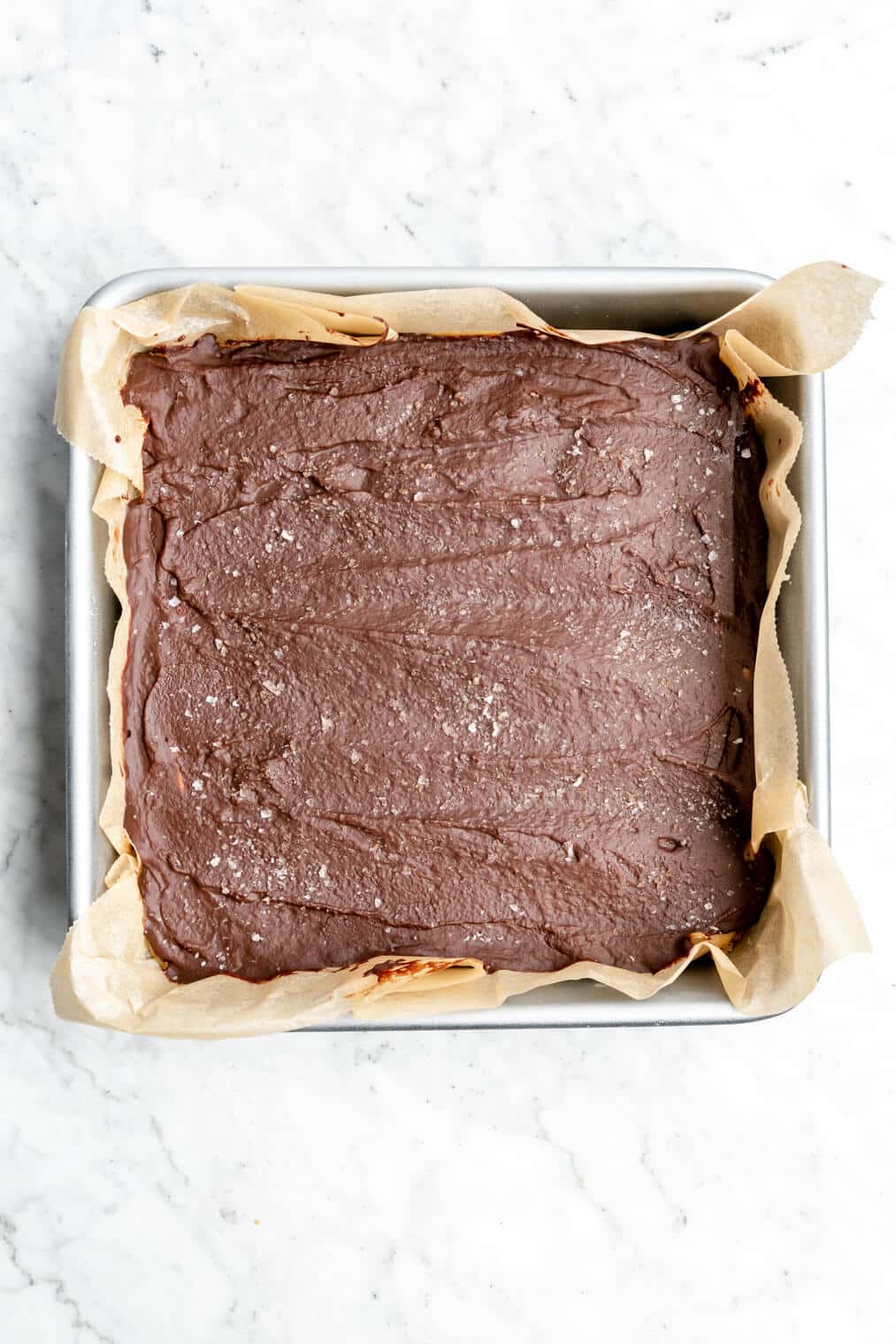 Millionaire bars with set chocolate ganache in an 8x8 pan lined with parchment paper.