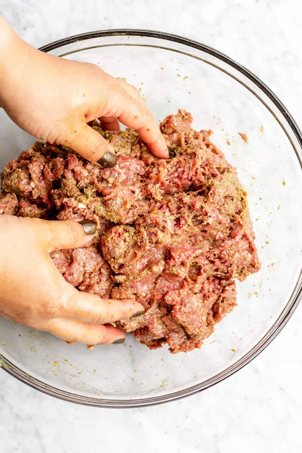 Hands mixing ground beef mixture in a glass bowl.