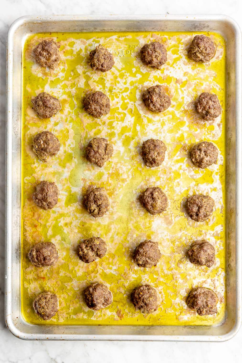 Six rows of 4 meatballs each baked on a rimmed baking sheet.