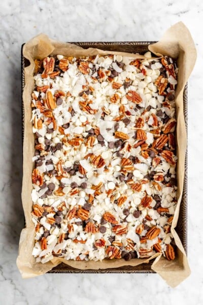 Layers of chocolate chips, white chocolate chips, pecans, and coconut in a 9x13 pan lined with parchment paper.