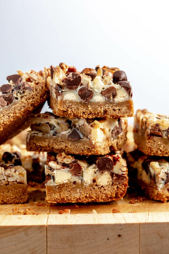 Stack of seven layer magic bars stacked 3 high on a wooden cutting board with a white background. 