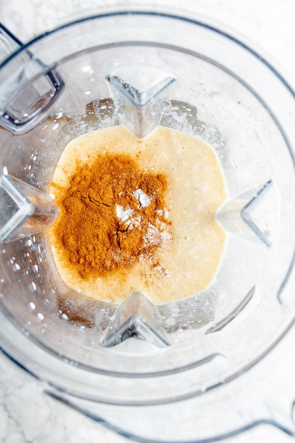 Spices and egg added to a blender pitcher that contains blended banana and milk.