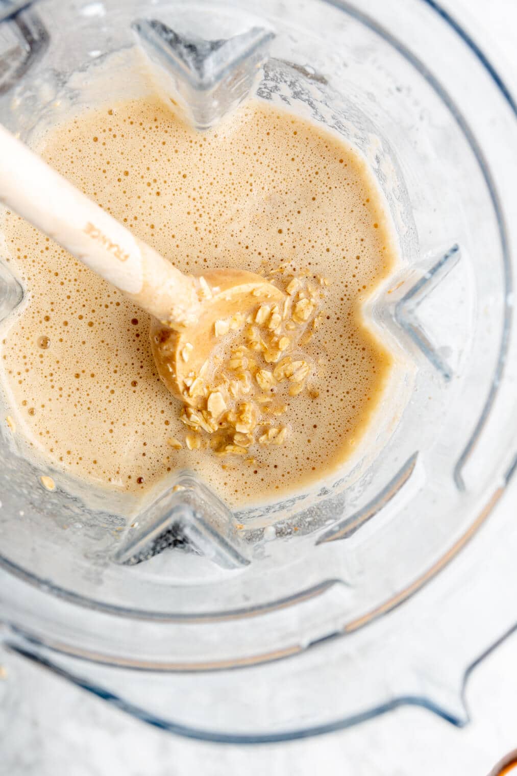 Spatula in a blender pitcher with soaked oats in a liquid mixture.