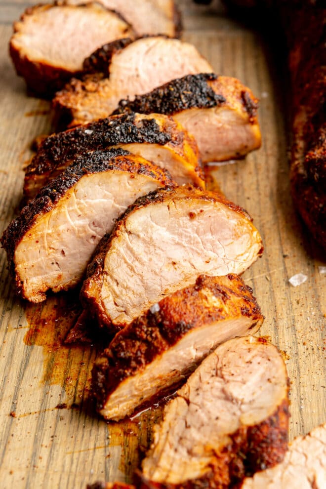 Up close photo of sliced pork tenderloin on a wooden cutting board.