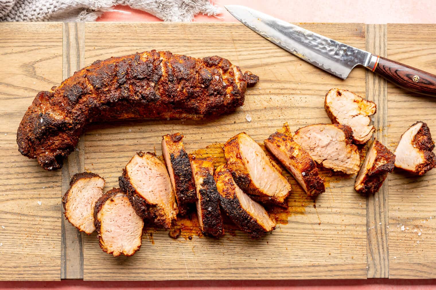 A rectangle, wooden cutting board with two roasted pork tenderloins. One is sliced into medallions, and the other is whole. Both have a dark chili rub on the exterior.