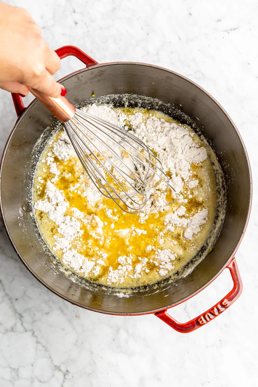 Hand whisking melted butter and flour together in a large dutch oven.