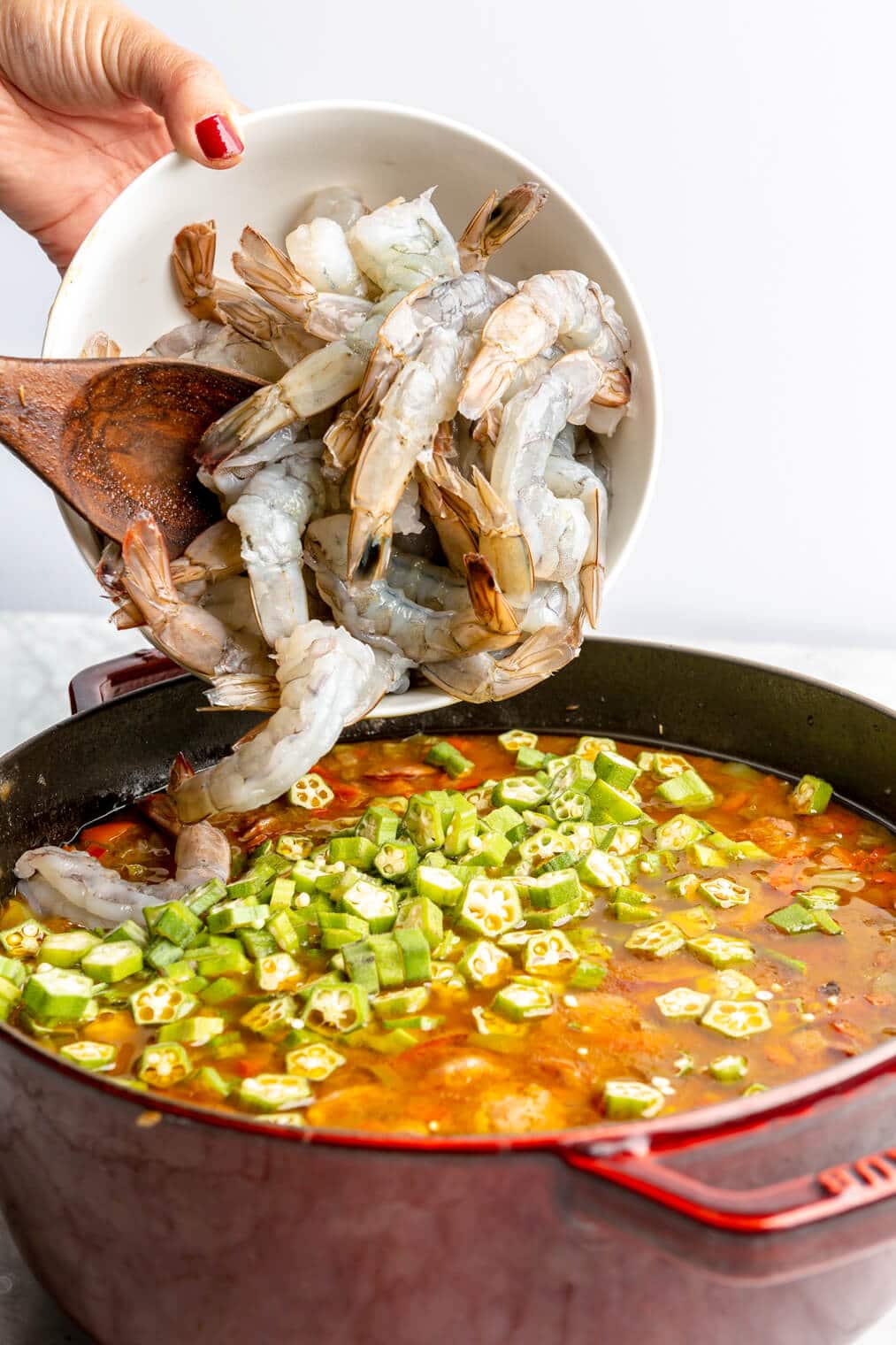 Raw shrimp added into gumbo ingredients in a large dutch oven.