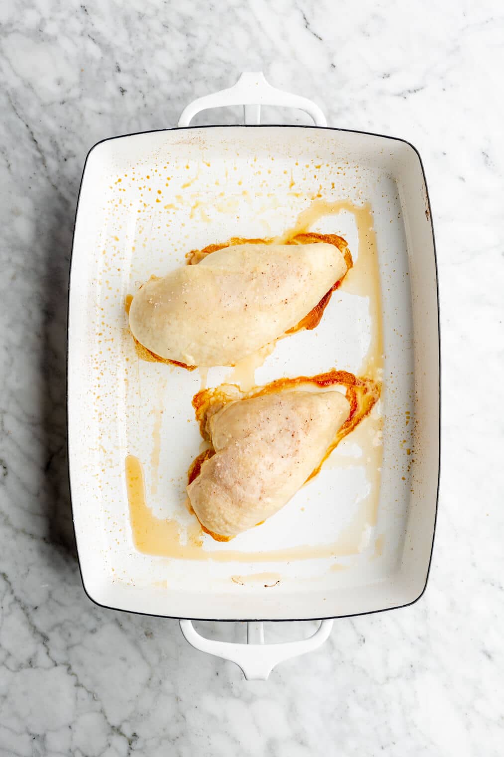 Top down view of two baked chicken breasts in a white casserole dish.