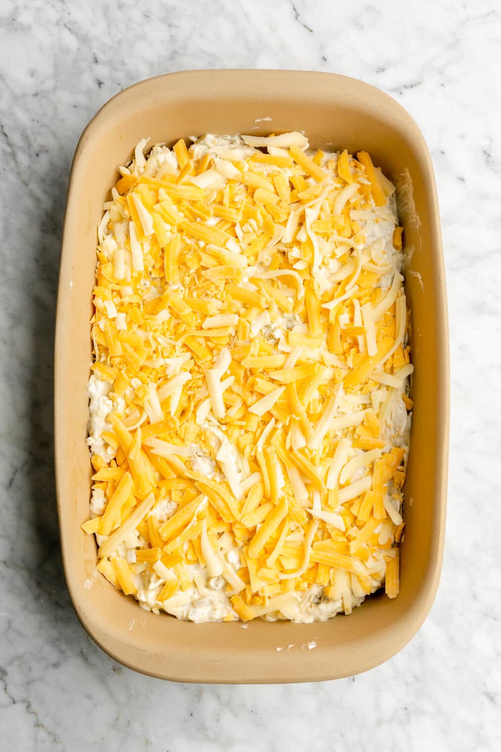 Layered green chili casserole topped with shredded cheese in a casserole dish.