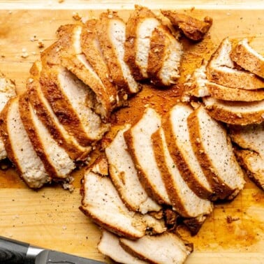 Sliced, sous vide chicken breast on a wooden cutting board. The chicken is moist and juicy and has a dark, molasses colored rub.