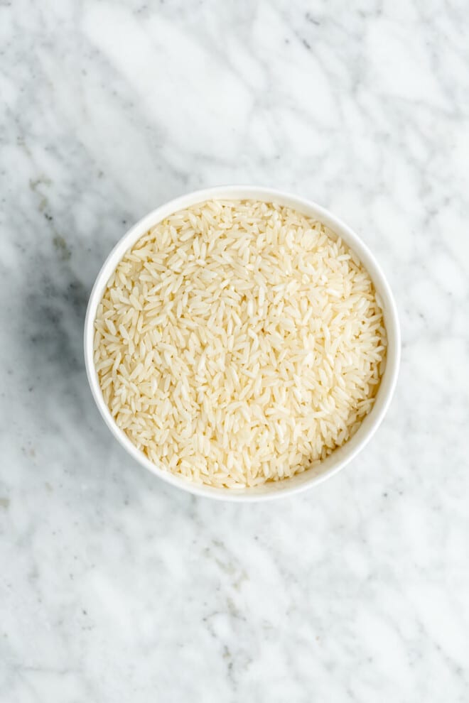Top down view of uncooked rice in a white bowl.