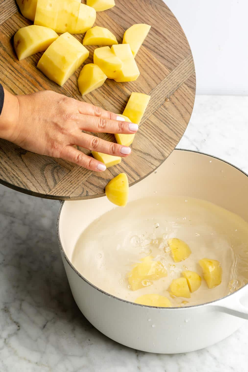 Hand adding potatoes to a pot of water.