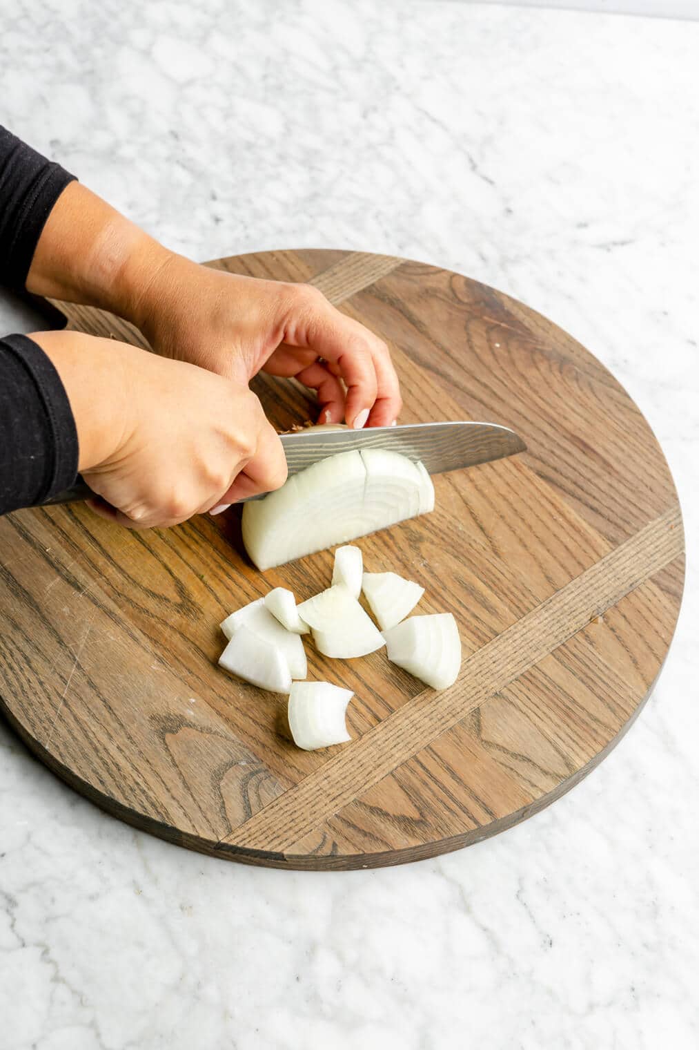 Hand slicing white onion into pieces.