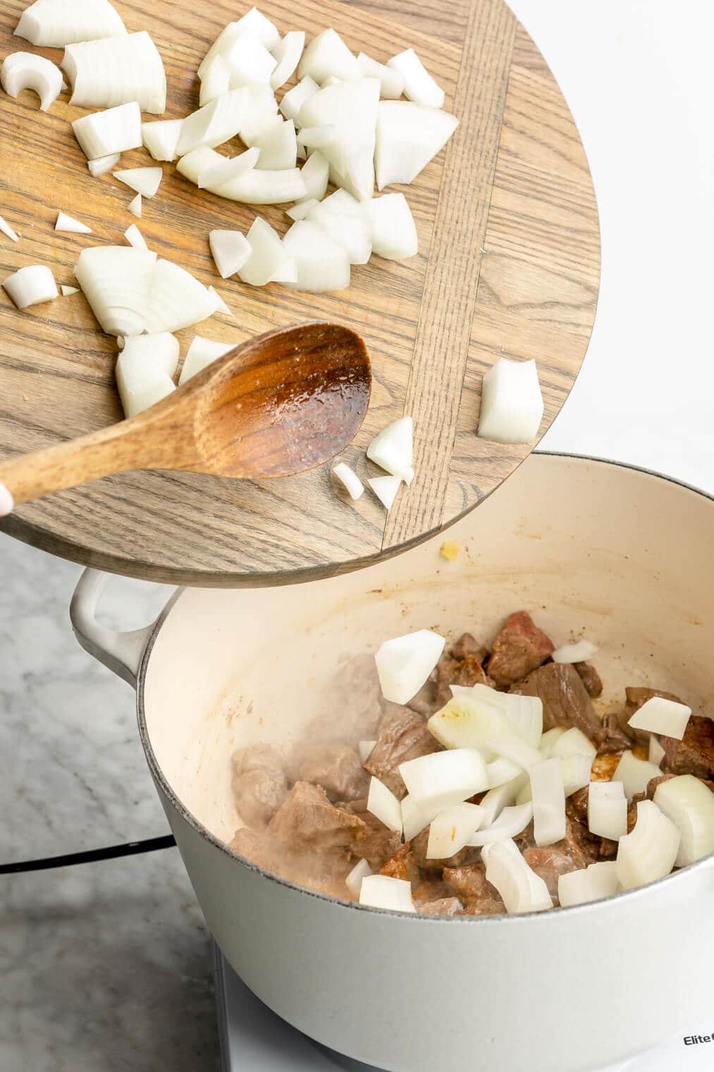 Wooden spoon adding diced onions to the pan.
