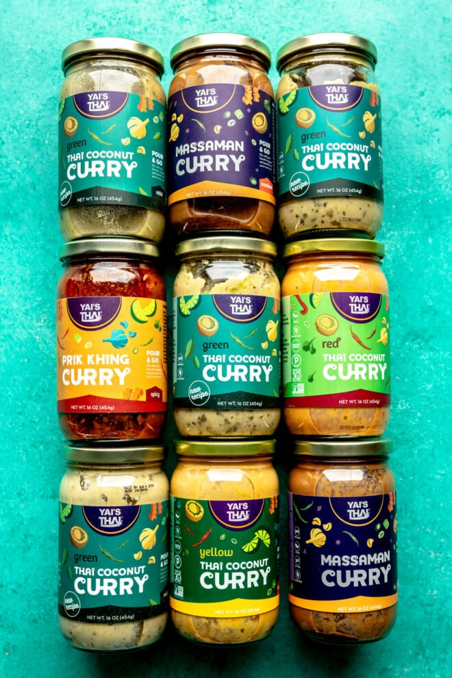 Yai's Thai curry sauces in three rows of three jars on a teal surface.