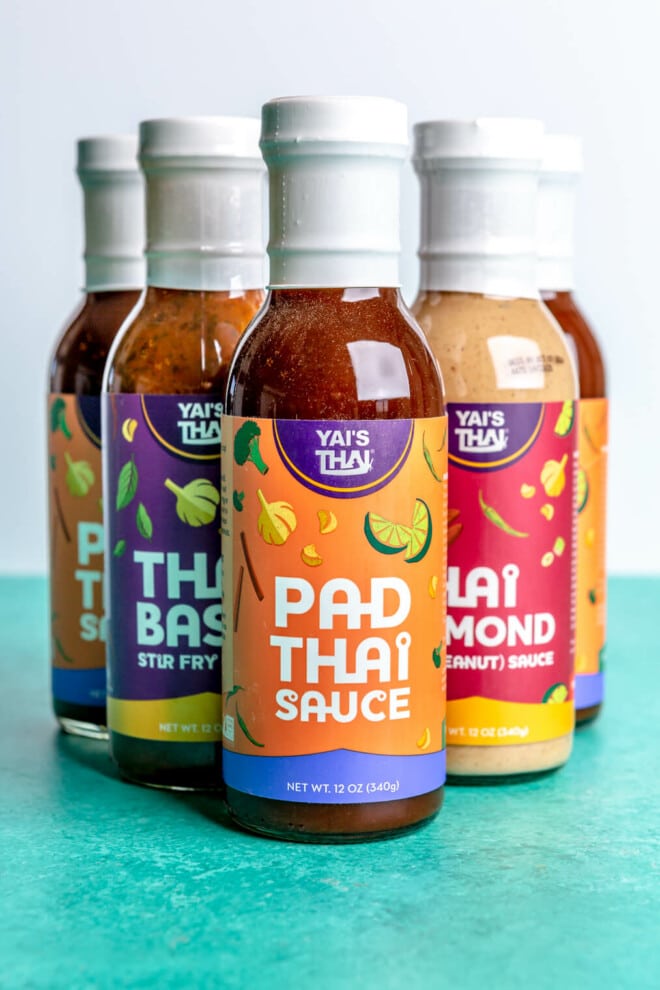 Yai's Thai sauce and marinade jars in a triangle formation with Pad Thai sauce at the front on a teal surface.